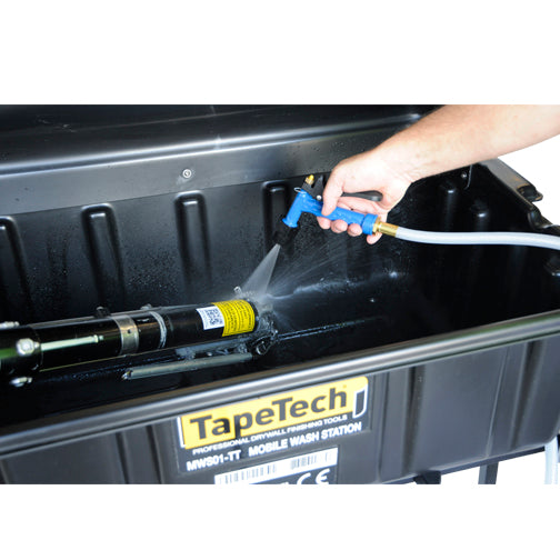 Close-up of a person using a TapeTech water sprayer to clean the end of a taper inside a black wash basin